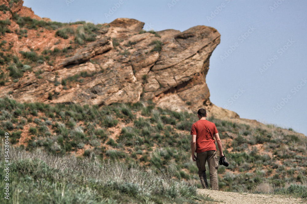 Man with camera in hand walking on the road in countryside to the mountain