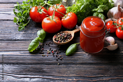 Composition of ketchup in jar and ingredients on wooden background