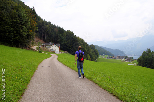 Travel to Sankt-Wolfgang, Austria. The young man are walking on a road between fields with the houses and the mountains on the background.