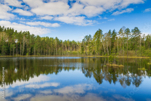 Clouds are reflected in the forest lake. Spring landscape. Masuria, Poland.