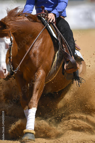 The close-up view of a rider in cowboy chaps and boots sliding the horse in the sand
