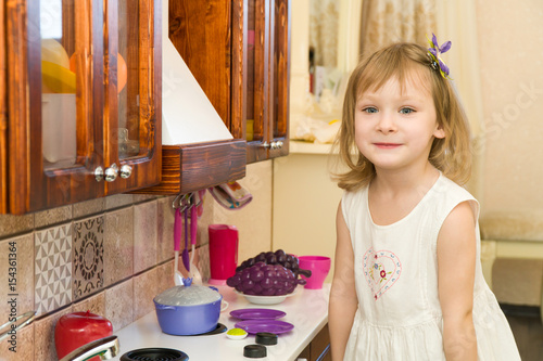 Active little preschool age child, cute toddler girl with blonde curly hair, shows playing kitchen, made of wood, plays in the kitchen photo