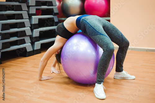 Pretty sexual straight fitness woman with musculat body lying on big ball in sport hall training indoor, horizontal picture