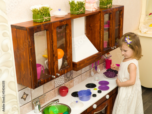 Active little preschool age child, cute toddler girl with blonde curly hair, shows playing kitchen, made of wood, plays in the kitchen photo