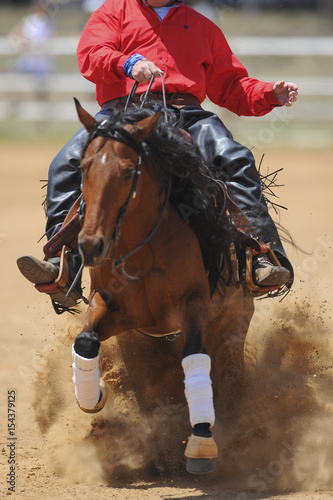 The front view of a rider in cowboy chaps and boots sliding the horse in the sand