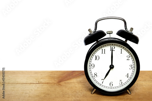 Classic alarm clock show time 7 o'clock and placed on a wooden plate on isolated white background and left copy space