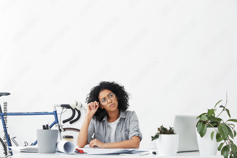 Φωτογραφία Shot of cute young entrepreneur with dark curly hair wearing shirt and round eyeglasses having thoughtful expression while planning her business meeting