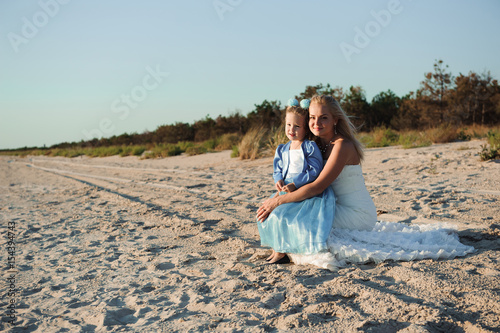 happy mother in the wedding dress with her daughter on the beach