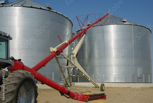 Storing Grain:  A tractor-driven auger transfers grain from a tray at ground level to the top of a storage bin on a farm in South Dakota.