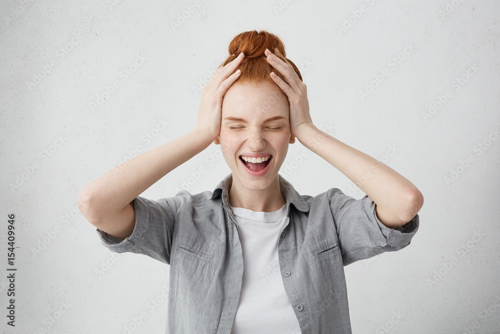 Emotional young woman with ginger hair and freckles closing eyes tight