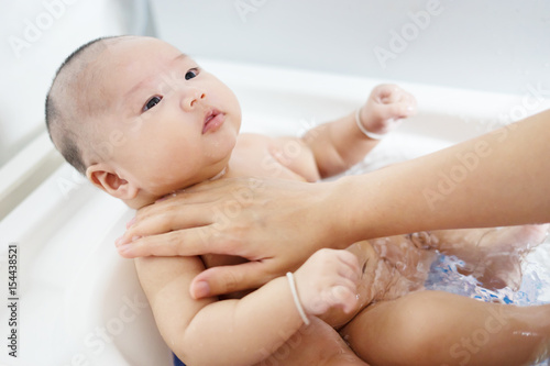Baby bath time concept,portrait of a baby is being bathed by his mother using tub at home,selective focus.