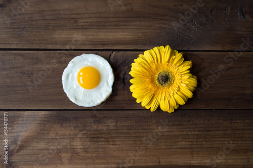 round shaped fried egg with yellow gerbera on dark wooden backgrond