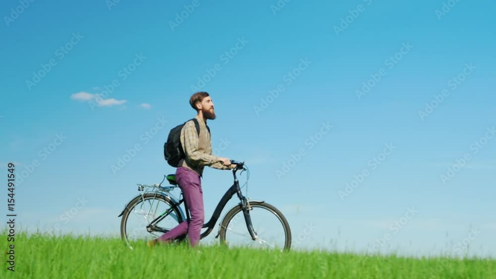 A young hipster man drives a bicycle through a green meadow. Beautiful scenery, picturesque place. A young hipster man drives a bicycle through a green meadow. Beautiful scenery, picturesque place.