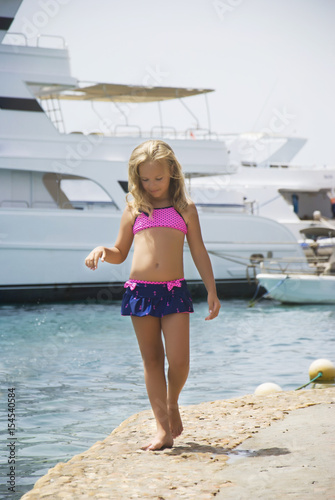 Beautiful girl strolls along the shore of the stone on the background of yachts