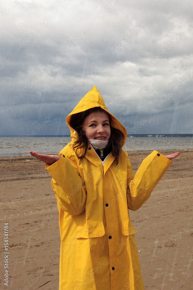 A young girl in a yellow raincoat is standing in the rain on the