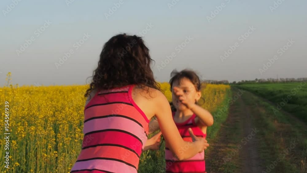 Happy mother hugging daughter. Woman with baby in nature in yellow flowers. The child runs to her mother.