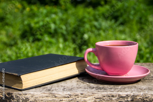 Coffee cup and old book on rustic wooden table outdoor