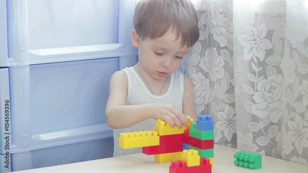 Boy builds a house out of colored blocks on a table Boy builds a house out of colored blocks on a table