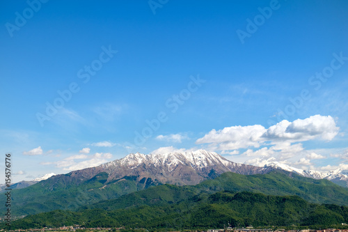 South view of piedmontese alps with snowy mountains and woods in spring from the Sanctuary of Madonna degli Alpini, in Cervasca, Cuneo, Italy. The town of Borgo San Dalmazzo is also visible. photo