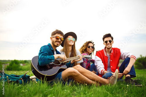 Group of friends enjoying party. The guy plays the guitar. Everyone has a great mood. Summer time.      © maxbelchenko