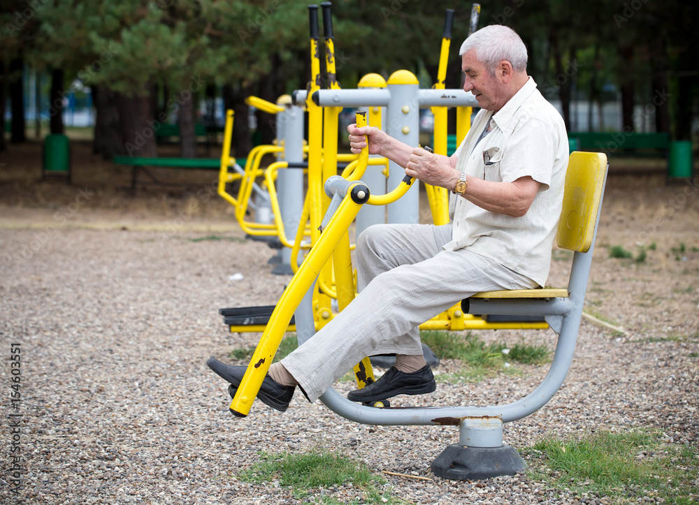 Old man making exercises on outdoor gym.