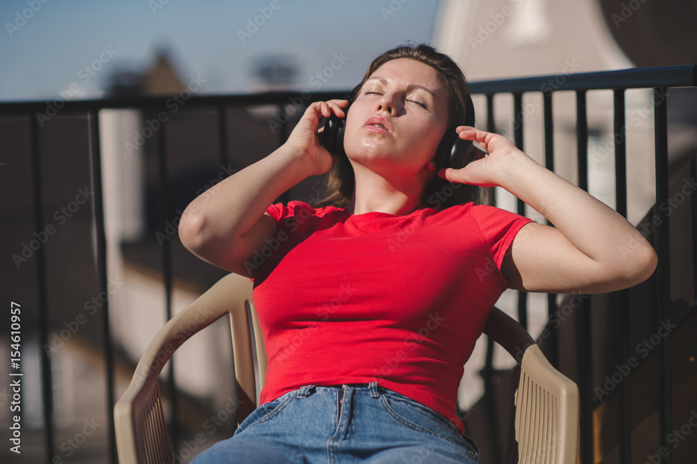 Beautiful girl in a red t-shirt and headphones. A girl on the balcony listening to music and is singing