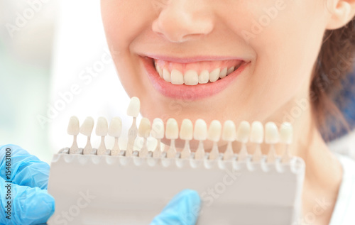 Dentist checking and selecting color of young woman's teeth