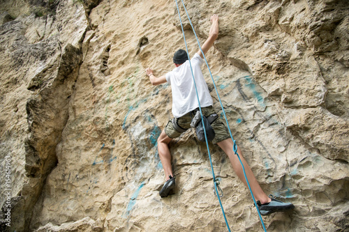 A young man is engaged in rock climbing on a steep rock without insurance