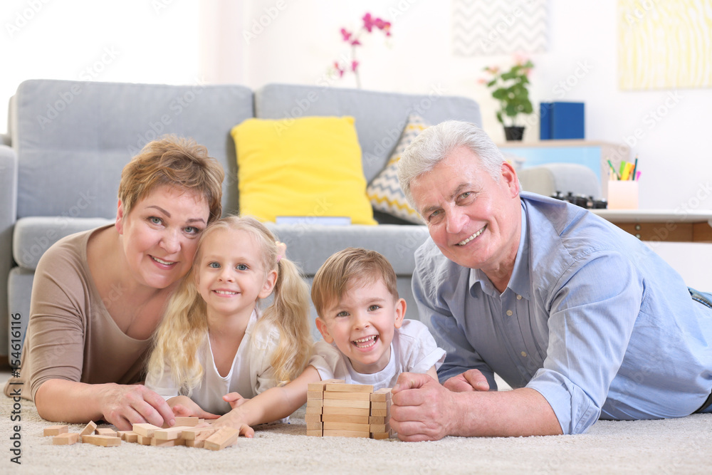 Φωτογραφία Happy senior couple and their grandchildren lying on floor and playing with wood