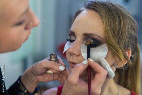 Make-up artist doing smoky eyes makeup to beautiful young girl in the studio