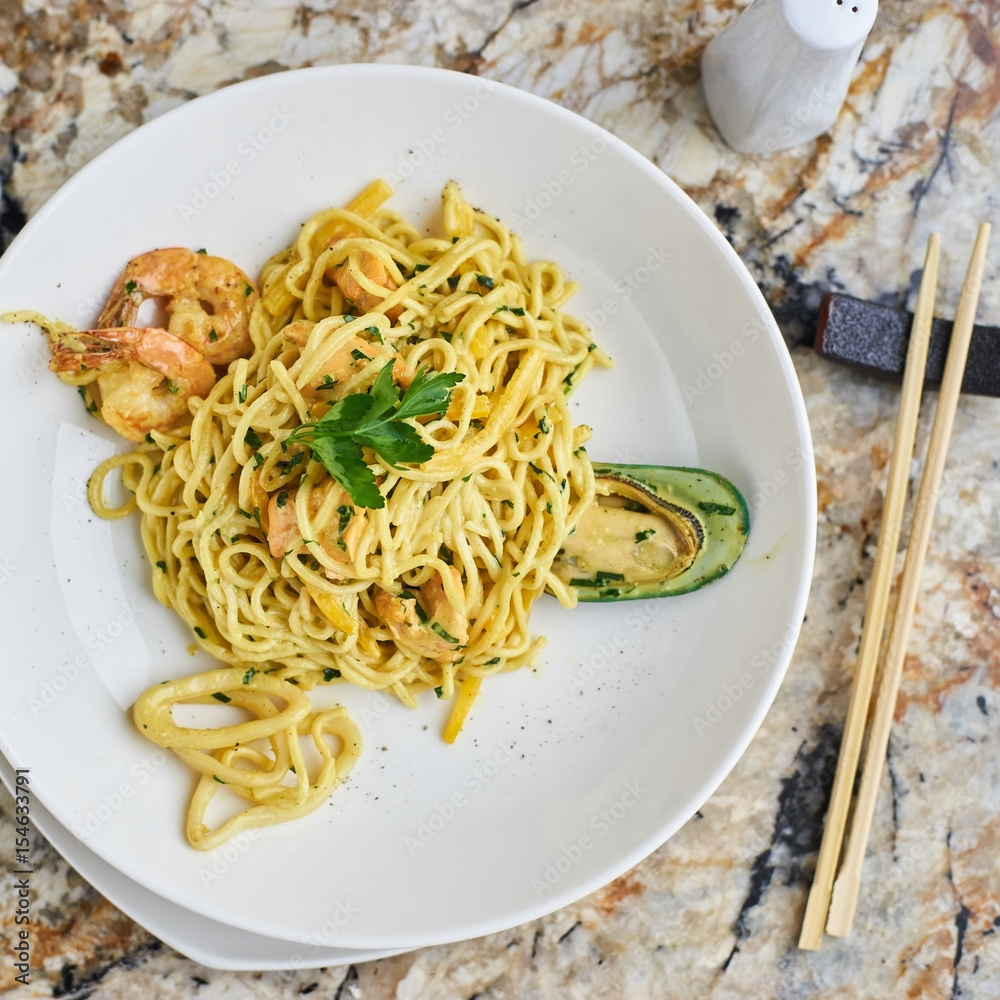 Flat egg noodles with seafood served in big white ceramic round plate with glass of white wine on marble table Flat egg noodles with seafood served in big white ceramic round plate with glass of white wine on marble table