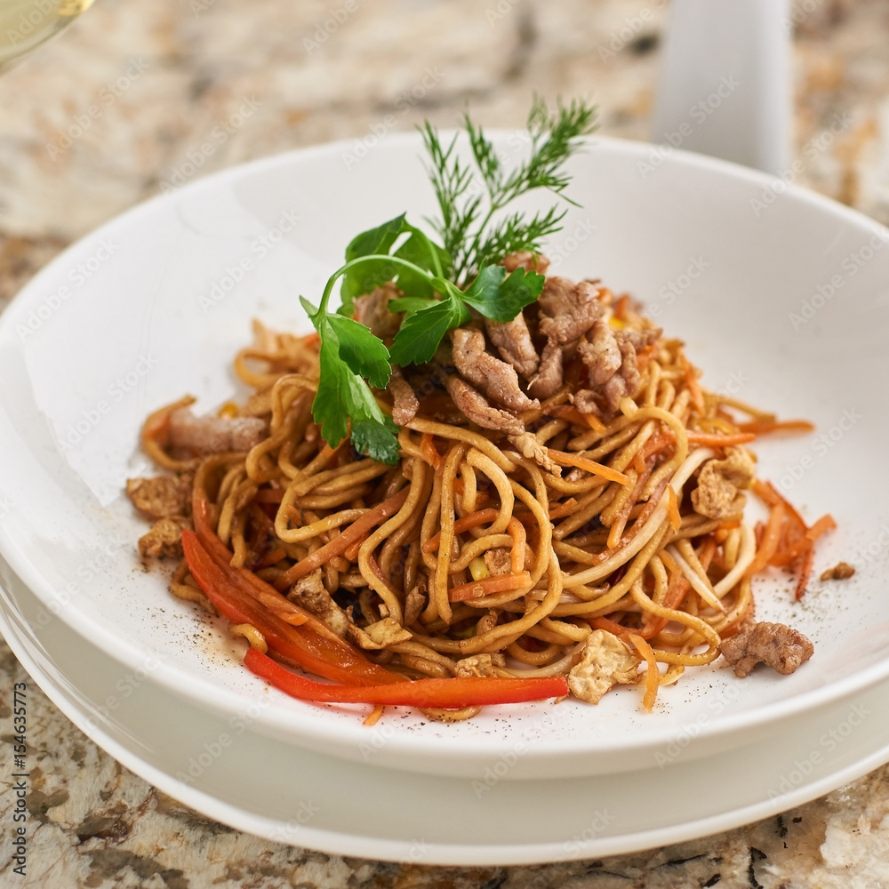 Flat egg noodles with pork slices served on white plate with white garlic and red spicy sauce