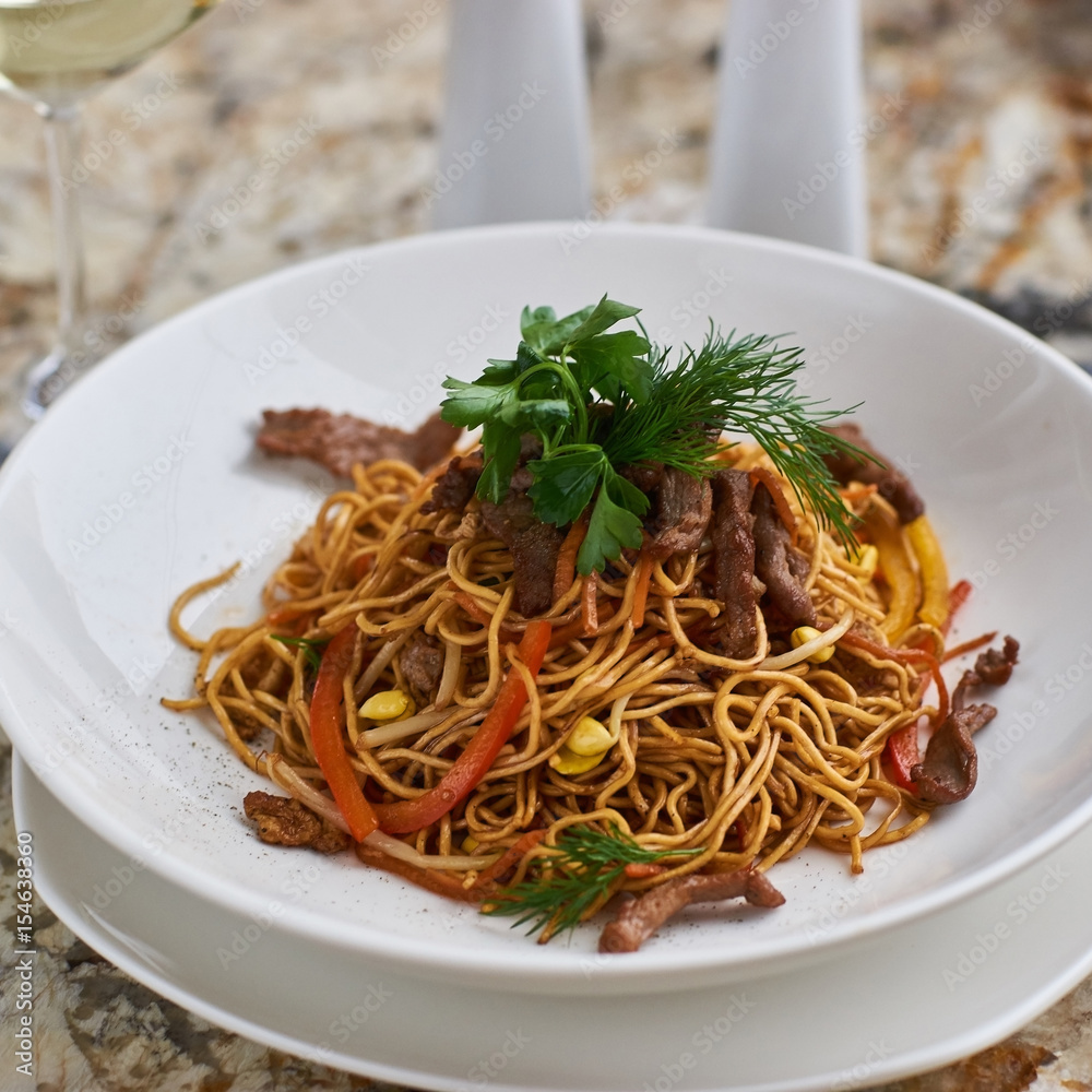Thin egg noodles with beef meat slices served on white plate with white