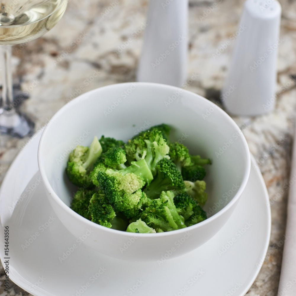 Steamed broccoli served in white bowl with glass of white wine on marble background Steamed broccoli served in white bowl with glass of white wine on marble background