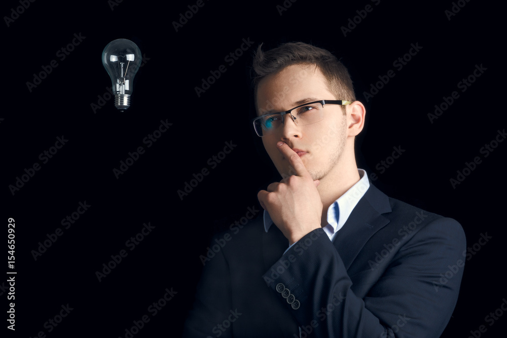 In search of a good idea. The businessman thinks. A man in a business suit on a black background thinks next to a light bulb. In search of a good idea. The businessman thinks. A man in a business suit on a black background thinks next to a light bulb.