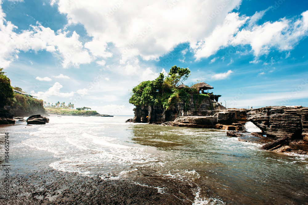Pura Tanah Lot. Unique hindu temple on a rock in the sea, Bali, Indonesia. Wide angle, dramatic sky with clouds and waves and swash in the foreground. Pura Tanah Lot. Unique hindu temple on a rock in the sea, Bali, Indonesia. Wide angle, dramatic sky with clouds and waves and swash in the foreground.