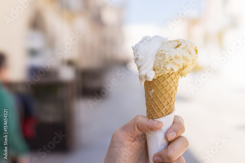 Close up focus of female hand holding melting delicious ice cream gelato with sun flare summer, Italy