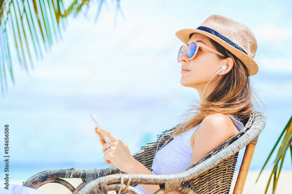 Young sexy woman with earphones using phone on the beach