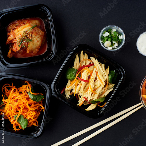 Korean cuisine. Set of salads on black background. Asparagus, korean carrot, kaktugi, fresh vegetable sticks and green onion. photo