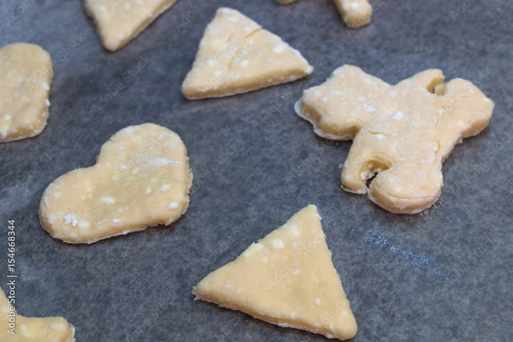 Cookie dough in different shapes lies on the baking sheet.