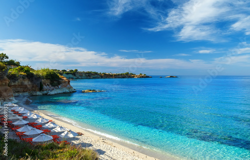 plaża z białym piaskiem i czystą błękitną wodą w pięknej zatoce z leżakami i parasolami, Kreta, Grecja