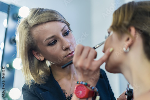 Make-up artist doing smoky eyes makeup to beautiful young girl in the studio