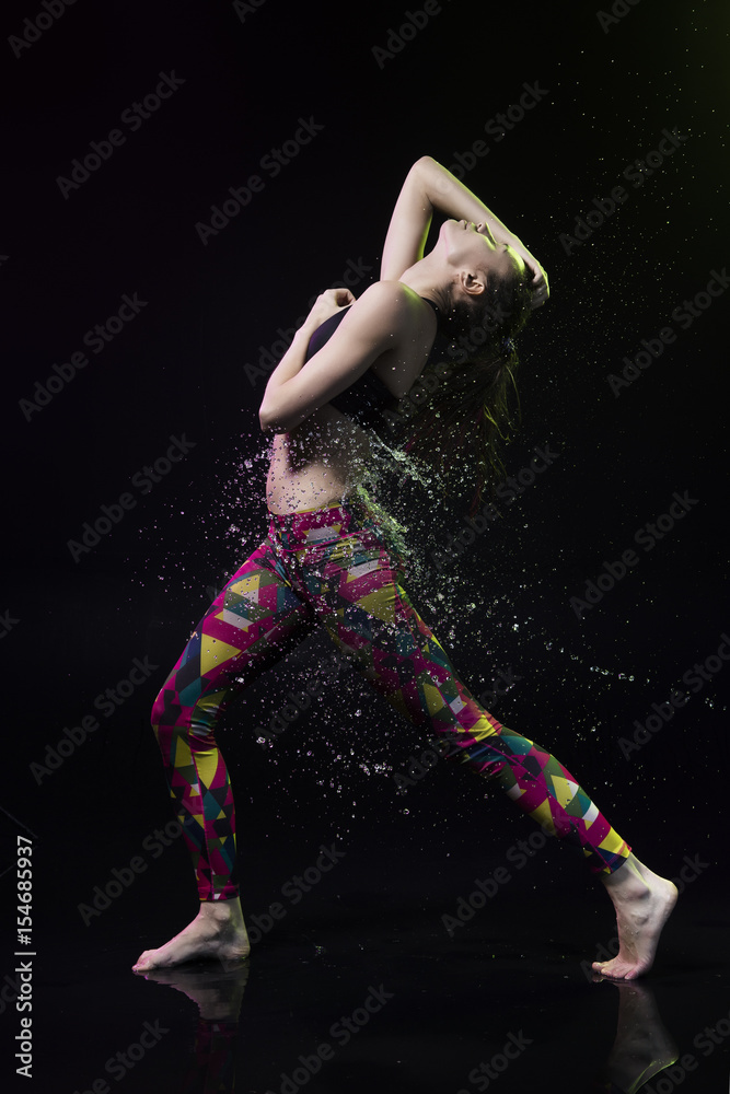 The girl dances on the floor covered with water on a black background and water splashes around her