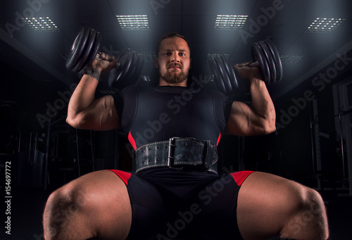 The athlete sits on a bench and does an exercise called military press photo