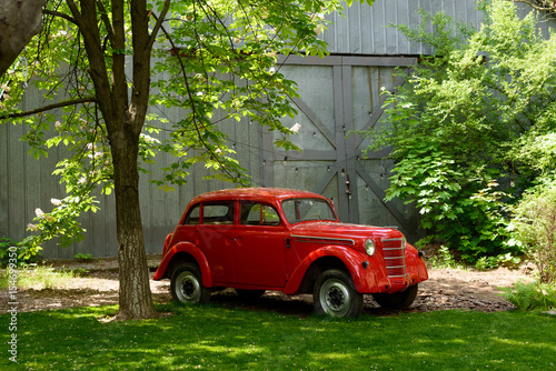 Red retro car in a garden amongst trees