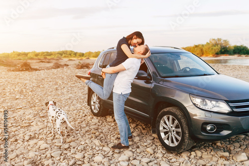 Happy traveler couple embrace near car with dog