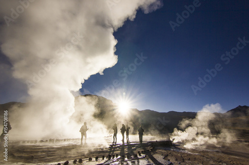 steam of geyser tatio against sun at sunrise with people standing
