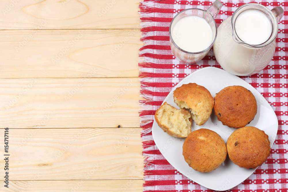 Glass jug pitcher of fresh milk with glass and muffins in a rustic setting on the wooden background with copy space. Top view. Glass jug pitcher of fresh milk with glass and muffins in a rustic setting on the wooden background with copy space. Top view.