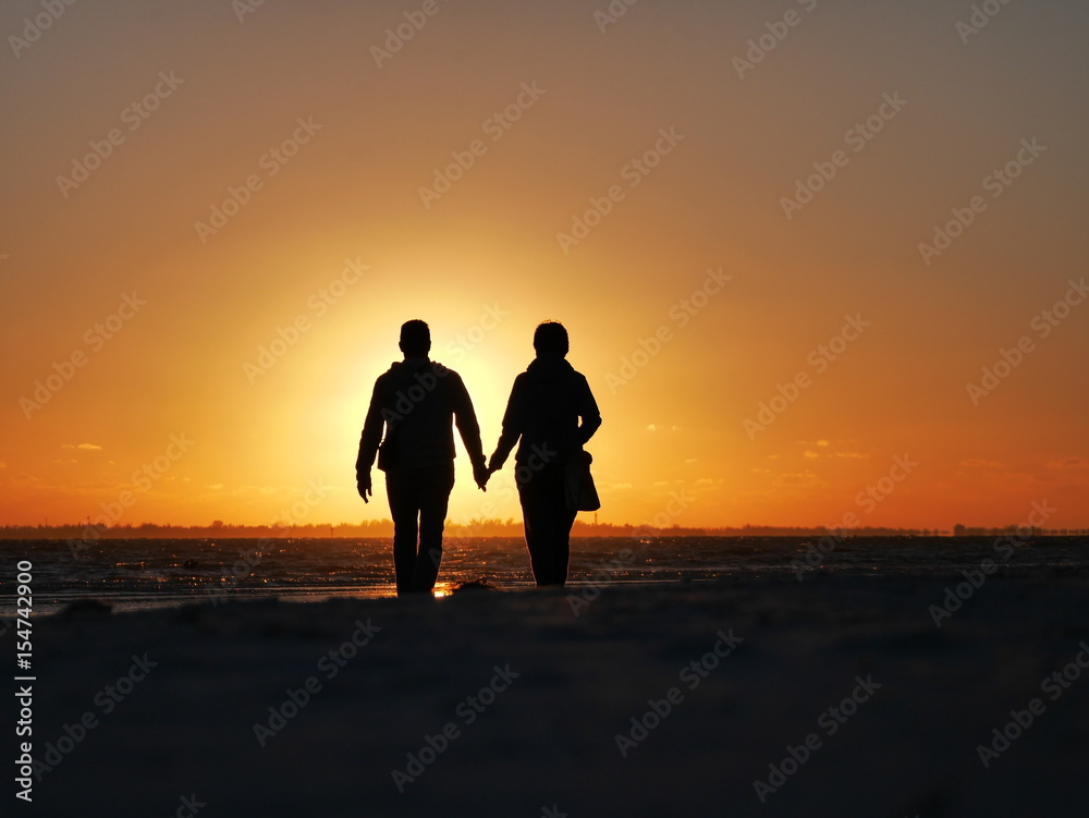 Ein Paar geht Händchen haltend der Sonne entgegen