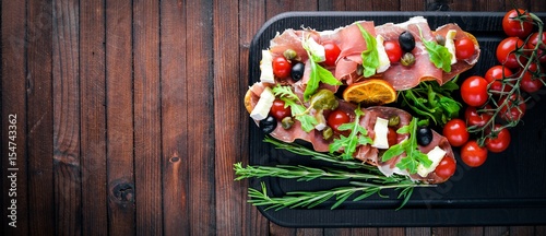 Fototapeta Naklejka Na Ścianę i Meble -  Bruschetta with meat, olives, herbs and parmesan cheese on bread. Cold snacks. Italian cuisine. On Wooden background.